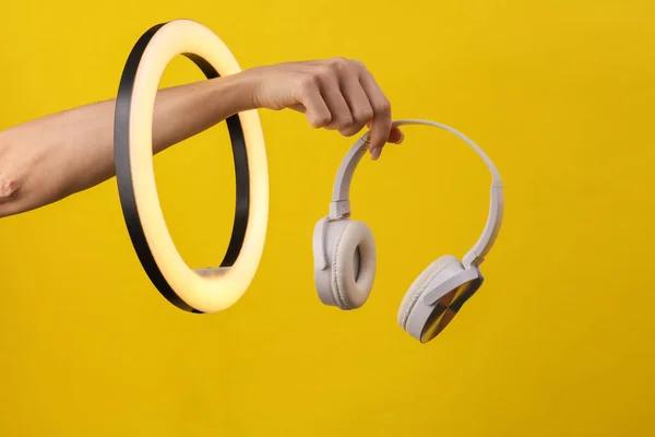 女人的手拿着白色的耳机 穿过黄底的引线环灯 创意创意 — 图库照片