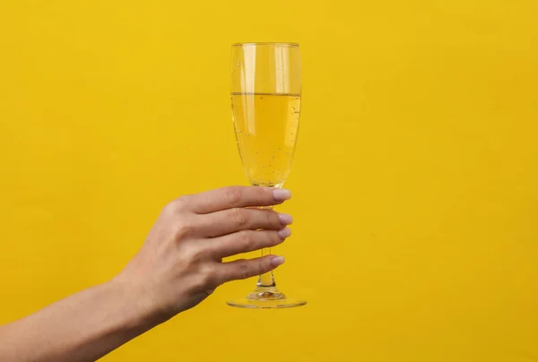 stock image Woman's hand holds champagne glass on yellow background. Creative idea.