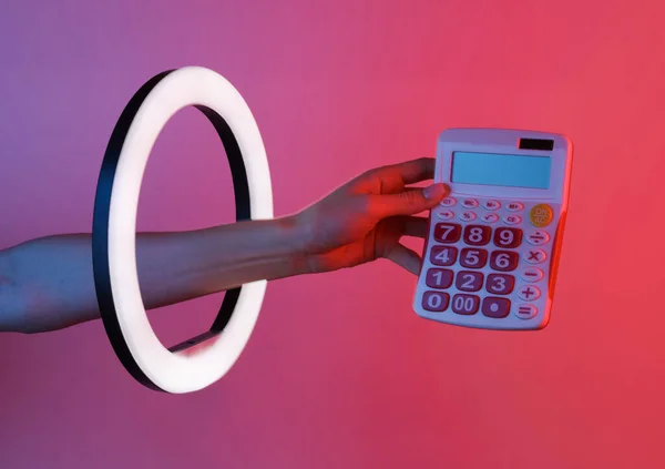 Woman\'s hand holds calculator through led ring lamp in red blue neon gradient light. Creative idea.