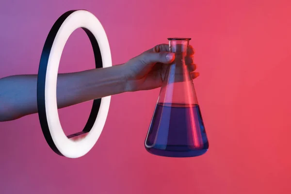 女性の手は 赤いネオングラデーションの光の中で鉛リングランプを通して化学実験室のフラスコを保持しています 創造的なアイデア — ストック写真