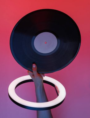 Kadının eli, kırmızı mavi neon renkli ışıkta, kurşun halkalı lamba aracılığıyla retro vinil plağı tutuyor. Yaratıcı bir fikir. Retro dalga