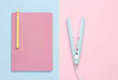 Mavi pembe arka planda not defteri olan mini saç düzleştirici. Üst görünüm