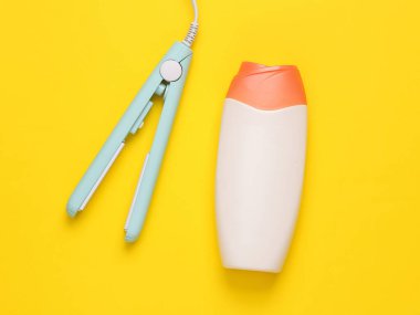 Sarı arka planda bir şişe şampuanla mini saç düzleştiricisi. Saç stili. Üst görünüm