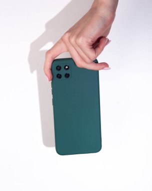 Kadının eli, beyaz arka planda yeşil bir koruyucu kapaklı akıllı telefonu tutuyor.