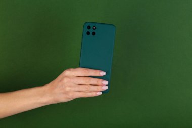 Kadının eli, yeşil arka planda yeşil bir koruyucu kapaklı akıllı telefonu tutuyor.