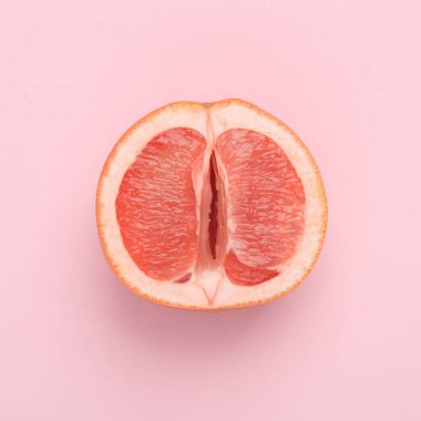 Gynecology, female intimate hygiene. Half of a ripe grapefruit symbolizing the female vagina on a pink background. Creative idea, allegory, fresh idea. Top view