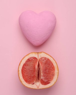 Gynecology, female intimate hygiene, love, sex concept. Half of ripe grapefruit symbolizing the female vagina and heart on a pink background. Top view