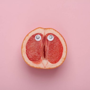 Pembe arka planda dik dik bakan yarım bir greyfurt. Asgari meyve kavramı