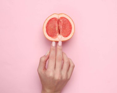 The mannequin's hand touches half of a grapefruit symbolizing the vagina. Pink background. Sex and fruit concept