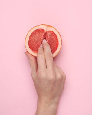 The mannequin's hand touches half of a grapefruit symbolizing the vagina. Pink background. Sex and fruit concept