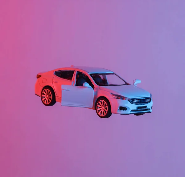 Toy car model floating in the air, isolated in blue-red neon gradient light. Levitating objects. Minimal concept