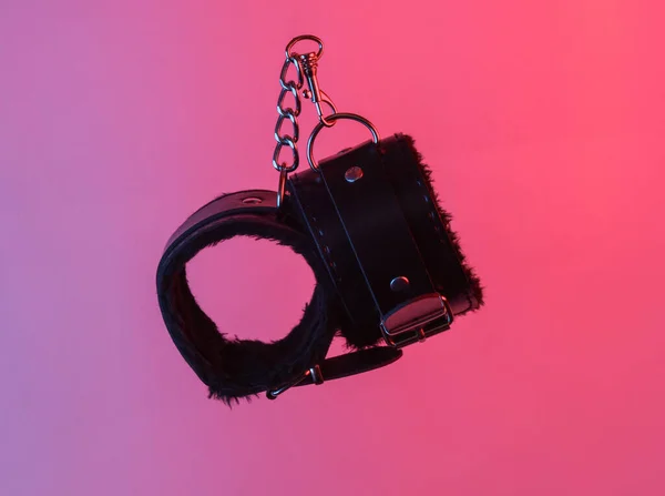 sex shop leather handcuffs floating in the air, isolated in blue-red neon gradient light. Levitating objects. Minimal concept. Sex games