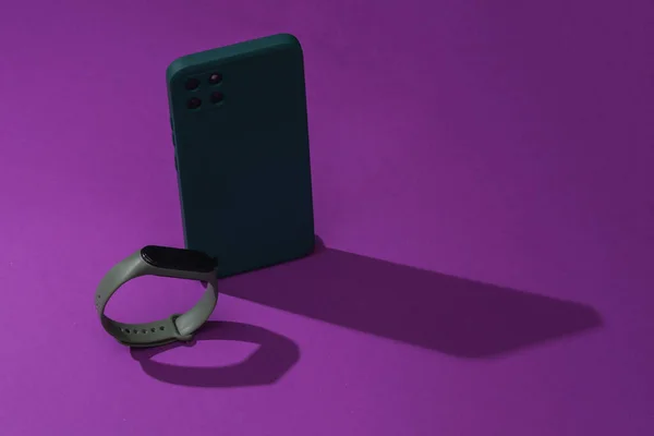 Modern smartphone and smart bracelet on purple background