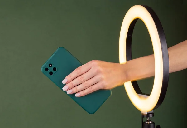 stock image Woman's hand hold smartphone through a ring LED lamp on a green background