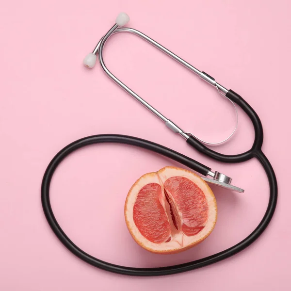 Diagnosis of female genital diseases concept. Half of a grapefruit symbolizing a female vagina and a stethoscope on a pink background