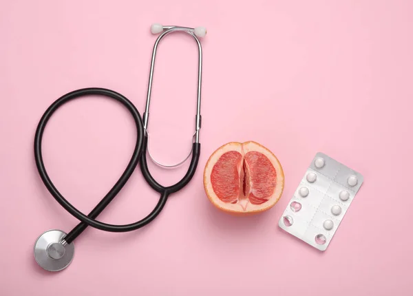 Diagnosis of female genital diseases concept. Half of a grapefruit symbolizing a female vagina pills and stethoscope on a pink background