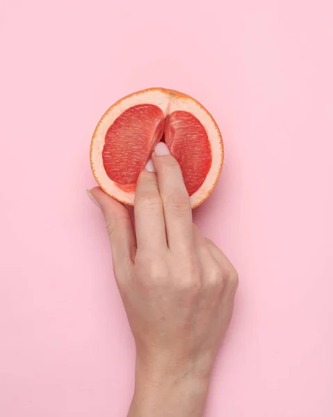 The mannequin\'s hand touches half of a grapefruit symbolizing the vagina. Pink background. Sex and fruit concept