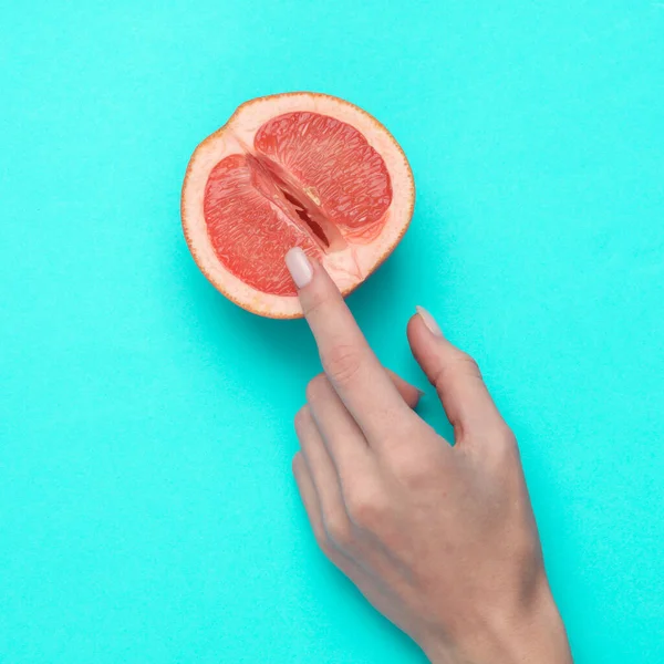 The mannequin\'s hand touches half of a grapefruit symbolizing the vagina. Blue background. Sex and fruit concept