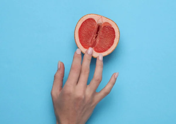 The mannequin's hand touches half of a grapefruit symbolizing the vagina. Blue background. Sex and fruit concept