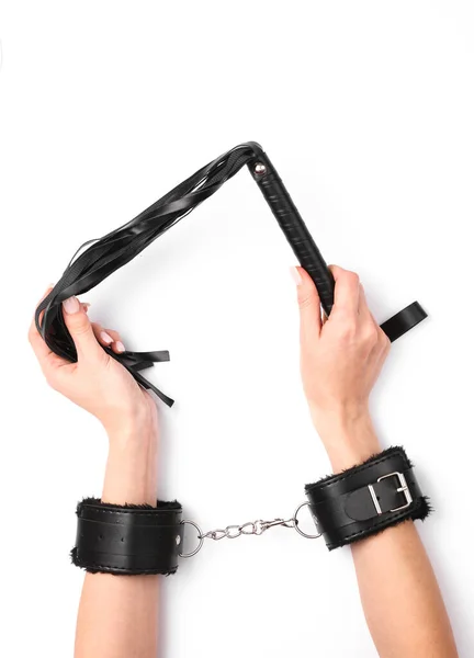 セックスショップの革の手錠で女性の手は白い背景に鞭を保持します セックスゲーム — ストック写真