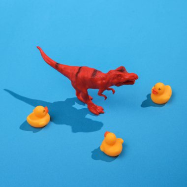 Tyrannosaurus ve parlak mavi arka planda lastik ördekler ile yaratıcı bir düzen. Görsel trend. Minimalist estetik, gölgeli bir hayat. Yeni fikir.