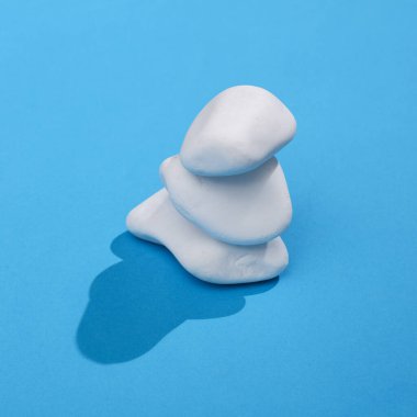 Bir yığın çakıl taşı olan yaratıcı bir düzen. Gölgeli parlak mavi bir arka plan. Görsel trend. Uyum kavramı. Minimalist estetik natürmort. Yeni fikir.