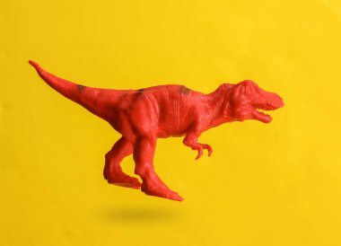 Plastik tyrannosaurus, sarı arka planda, gölgeli havada süzülüyor.