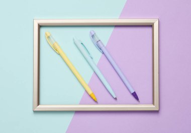 Pastel arka planda altın çerçeveli üç kalem. Üst görünüm