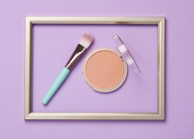 Pastel arka planda altın çerçeveli toz ve makyaj fırçası. Asgari güzellik kavramı