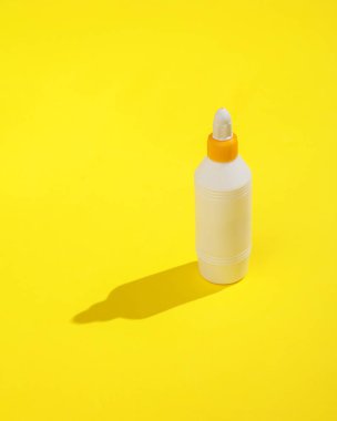 Sarı arka planda uzun gölgeli bir şişe yapıştırıcı. Minimalist fotoğraf