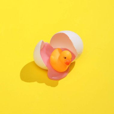 Kırık tavuk yumurtası kabuklu lastik ördekli yaratıcı bir düzen. Parlak sarı arka plan ve gölge. Görsel trend. Paskalya taahhüdü. Minimalist estetik natürmort. Yeni fikir.
