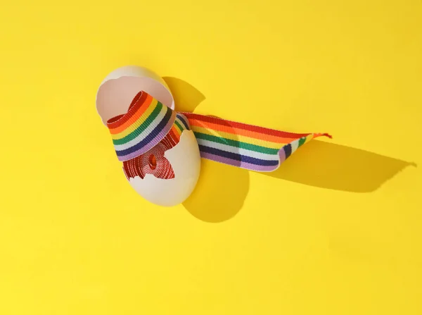 Creative layout with rainbow ribbon in eggshell on bright yellow background. Visual trend. LGBT concept. Minimalistic aesthetic still life with shadow. Fresh idea