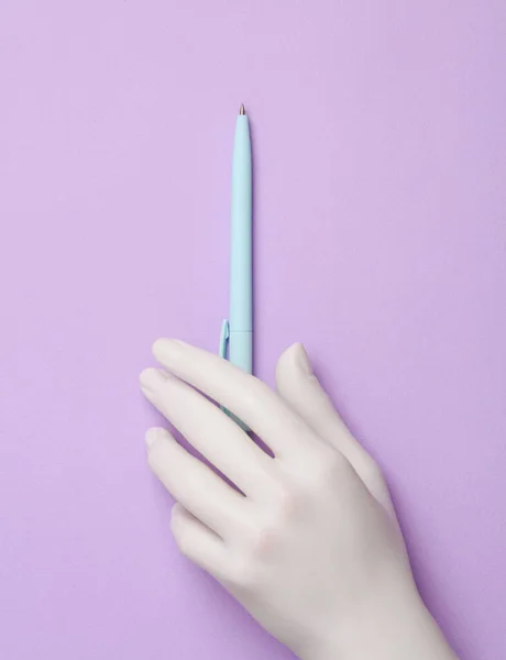 Plastic hand holding pen on pastel background