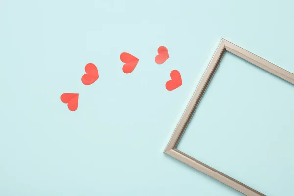 Empty gold frame with hearts on a pastel blue background. Love concept