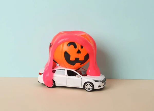 Creative halloween layout, car model with neon slime and bucket pumpkin on two tone dark background. Visual trend. Trick or treat