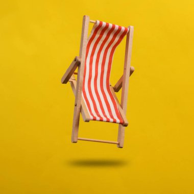 Güverte sandalyesi sarı arka planda, gölgeli havada süzülüyor.