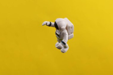 Oyuncak astronot modeli sarı arka planda anti yerçekiminde uçuyor.