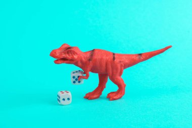 Oyuncak kırmızı dinozor tyrannosaurus rex turkuaz zemin üzerinde zar atıyor. Minimalizmin yaratıcı düzeni