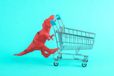 Turkuaz arka planında süpermarket tramvayı olan oyuncak kırmızı dinozor tyrannosaurus rex. Minimalizmin yaratıcı düzeni