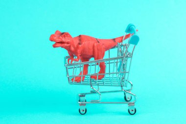 Turkuaz arka planında süpermarket tramvayı olan oyuncak kırmızı dinozor tyrannosaurus rex. Minimalizmin yaratıcı düzeni
