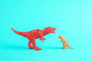 Turkuaz arka planda iki dinozor Tyrannosaurus Rex oyuncağı. Minimalizmin yaratıcı düzeni