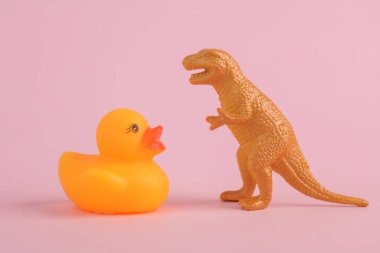 Oyuncak dinozor tyrannosaurus rex ve pembe arka planda plastik ördek. Minimalizmin yaratıcı düzeni