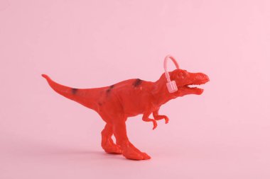 Oyuncak kırmızı dinozor tyrannosaurus rex pembe arka planda kulaklıkları var. Minimalizmin yaratıcı düzeni