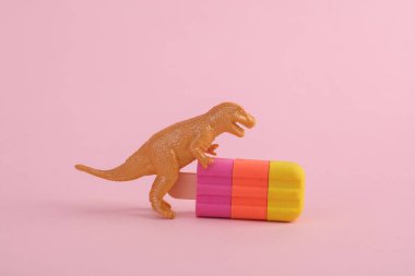Oyuncak dinozor tyrannosaurus rex ve pembe arka planda dondurma. Minimalizmin yaratıcı düzeni