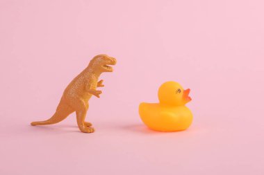 Oyuncak dinozor tyrannosaurus rex ve pembe arka planda plastik ördek. Minimalizmin yaratıcı düzeni