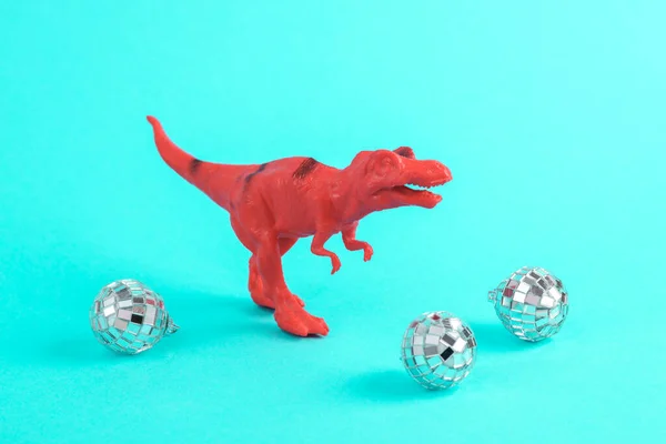 Toy red dinosaur tyrannosaurus rex with party disco balls on a turquoise background. Minimalism creative layout