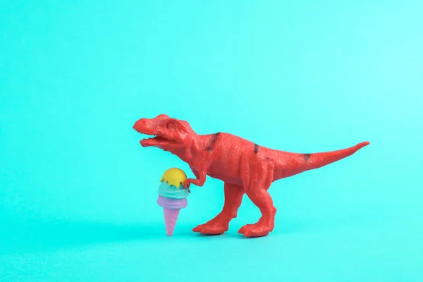 Toy red dinosaur tyrannosaurus rex with ice cream on a turquoise background. Minimalism creative layout