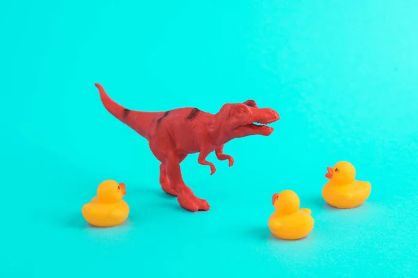 Toy red dinosaur tyrannosaurus rex with rubber ducks on a turquoise background. Minimalism creative layout