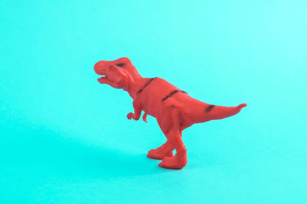 Toy red dinosaur tyrannosaurus rex on a turquoise background. Minimalism creative layout