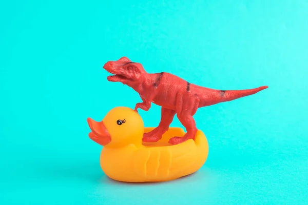 Toy red dinosaur tyrannosaurus rex with rubber duck on a turquoise background. Minimalism creative layout